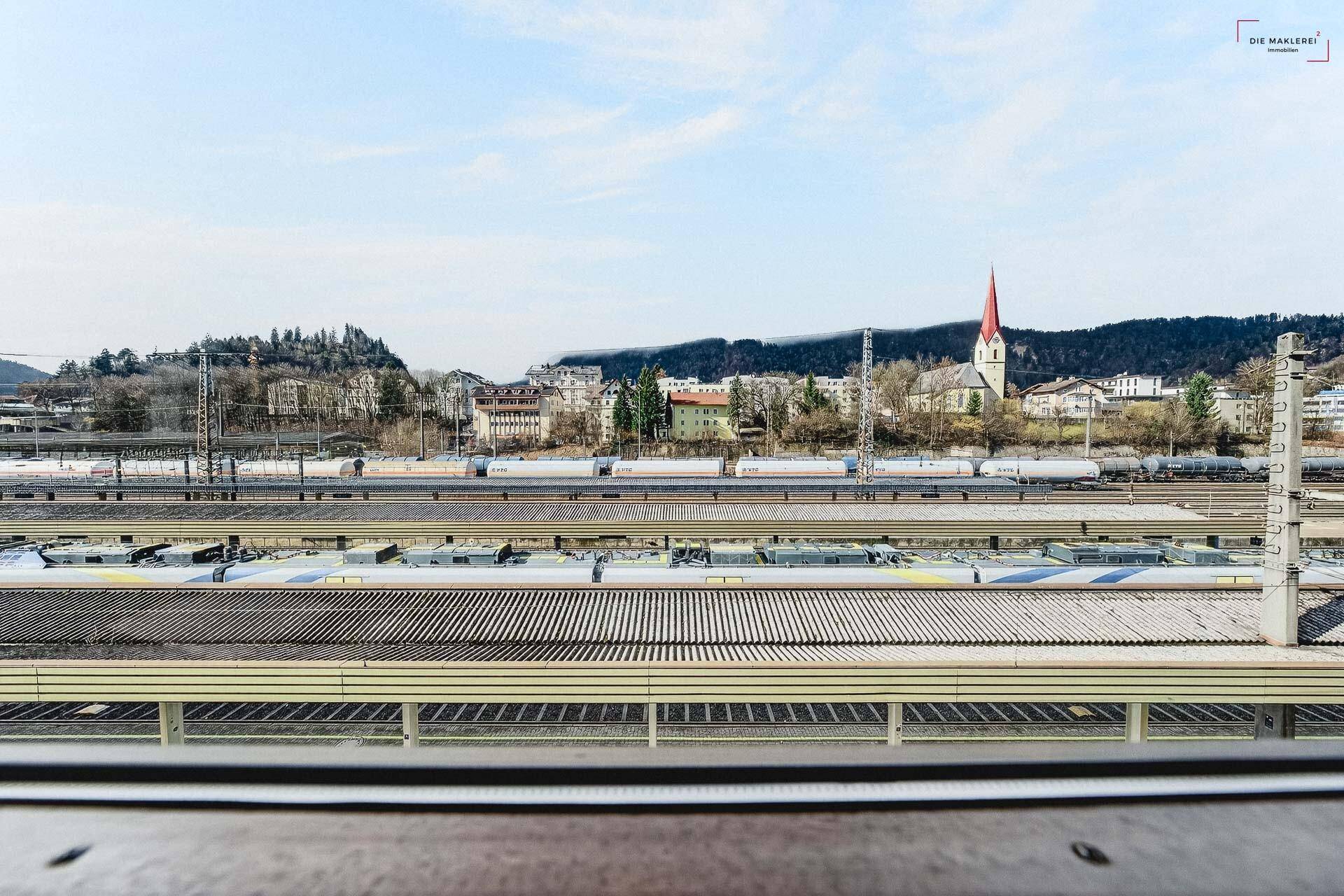Ausblick auf einen Bahnhof mit Zügen und die umliegende Stadt mit Bergen im Hintergrund.