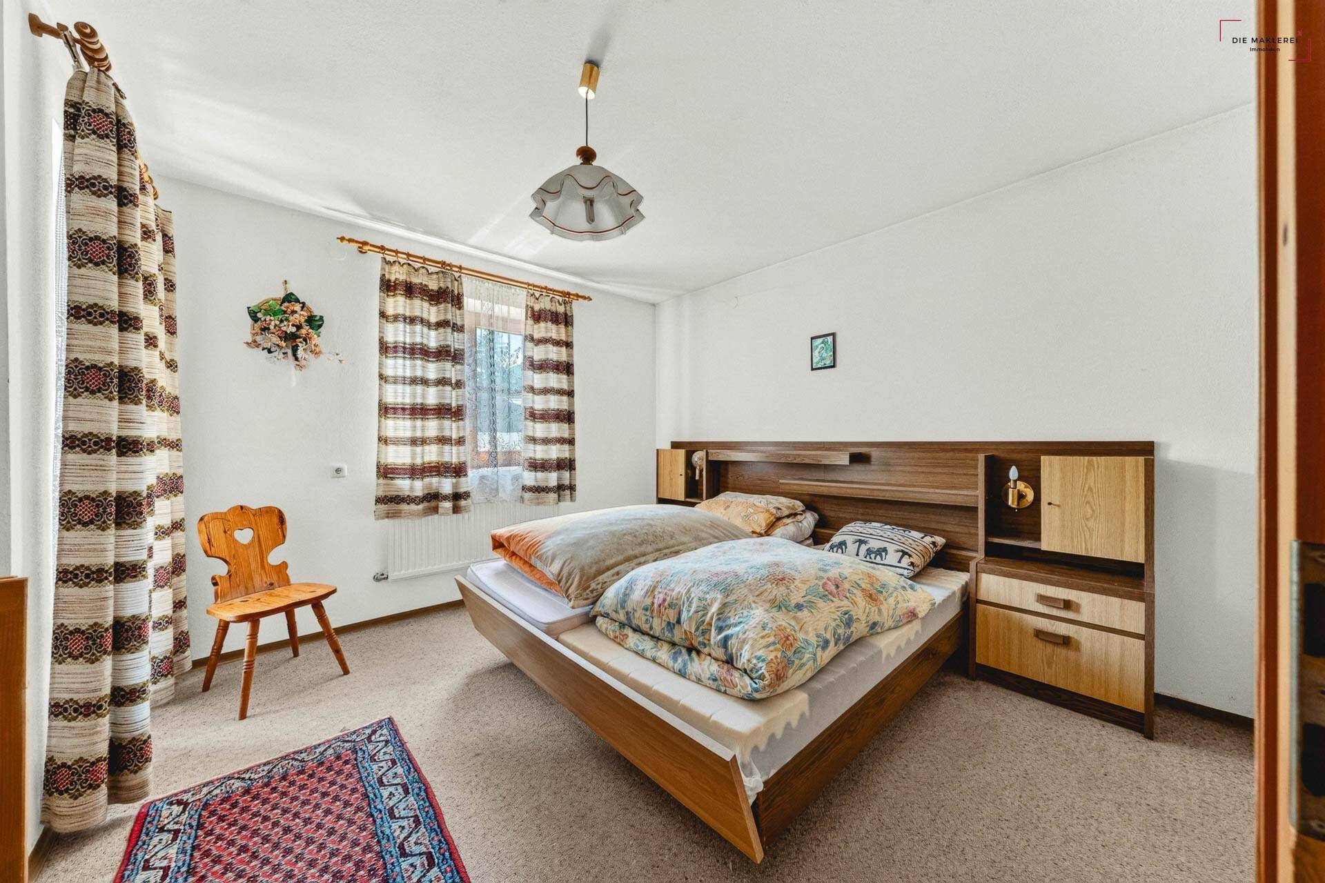 Schlafzimmer mit Teppichboden, Doppelbett und traditionellen Vorhängen an den Fenstern.