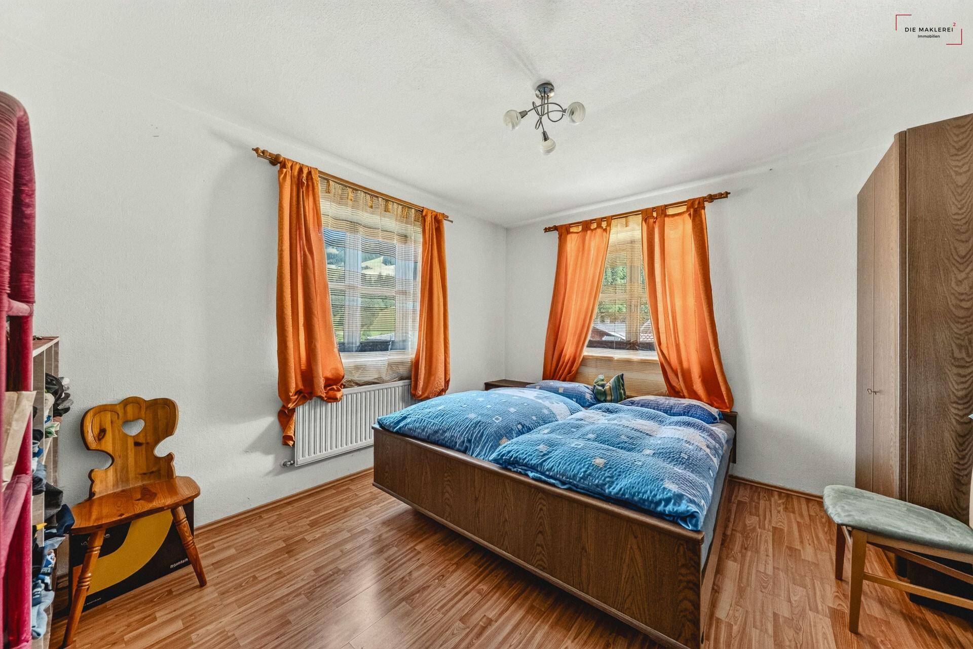 Schlafzimmer mit Holzboden, Doppelbett und orangefarbenen Vorhängen an den Fenstern.