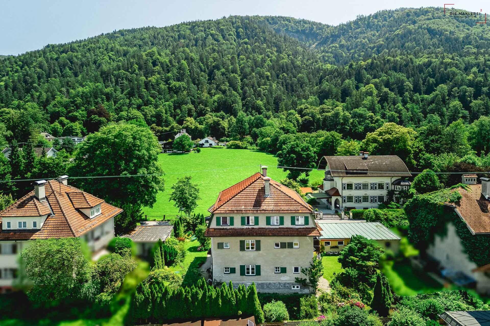 Luftaufnahme des Anwesens in einer grünen Wohngegend mit bewaldeten Hügeln im Hintergrund.