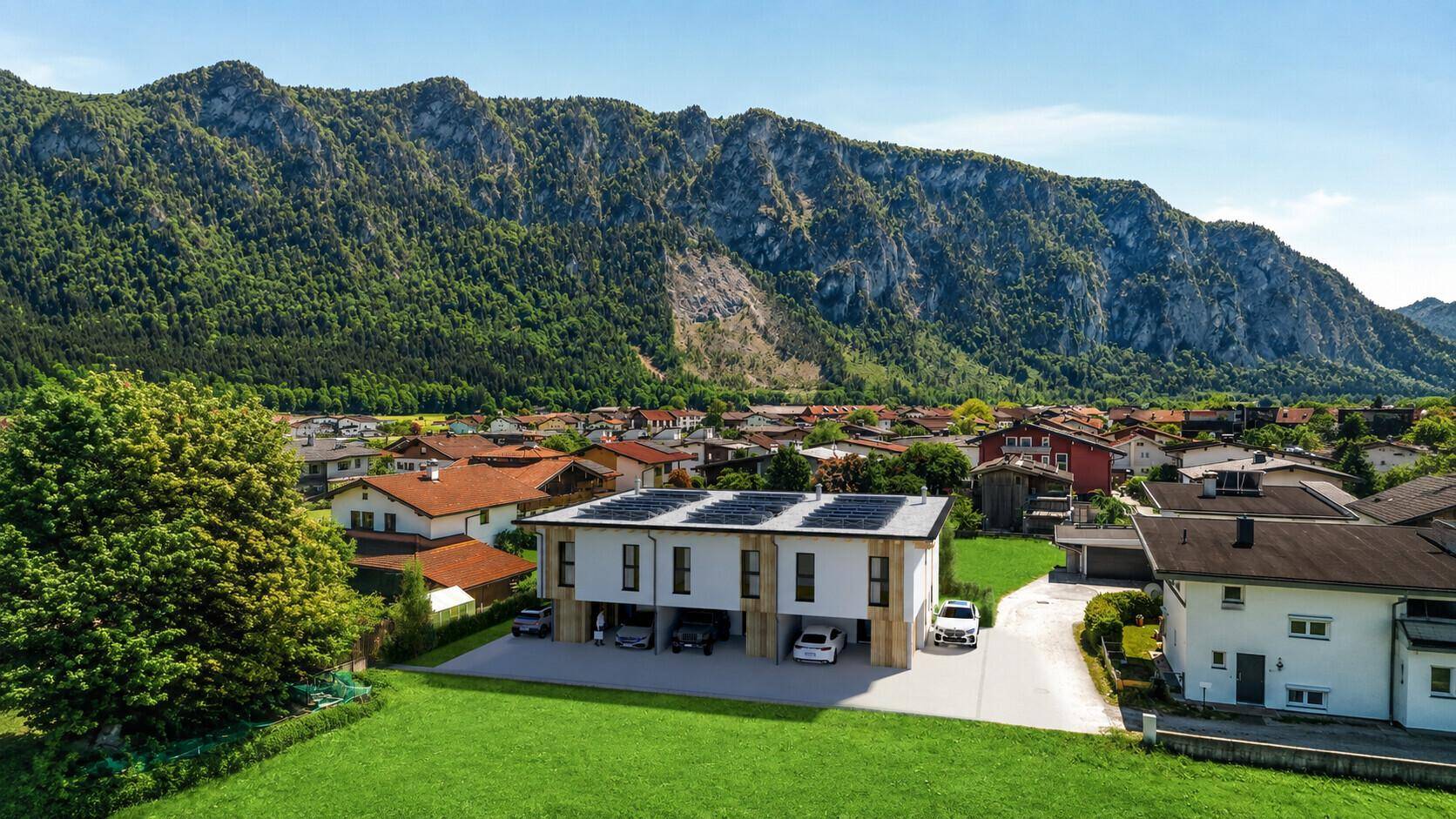 Panoramablick auf ein neues Wohngebäude mit Solarpaneelen vor einer beeindruckenden Bergkulisse.