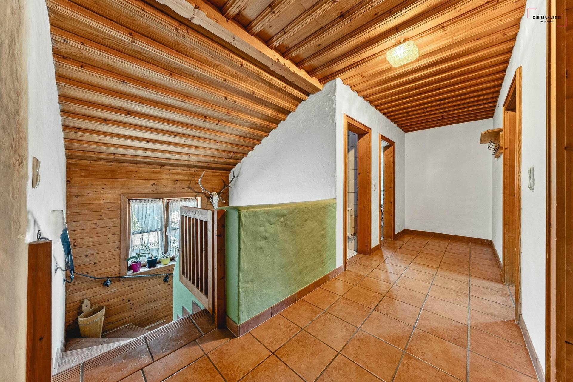 Obergeschoss-Flur mit Holzdecke, gefliestem Boden und Blick auf die Treppe mit Geländer.