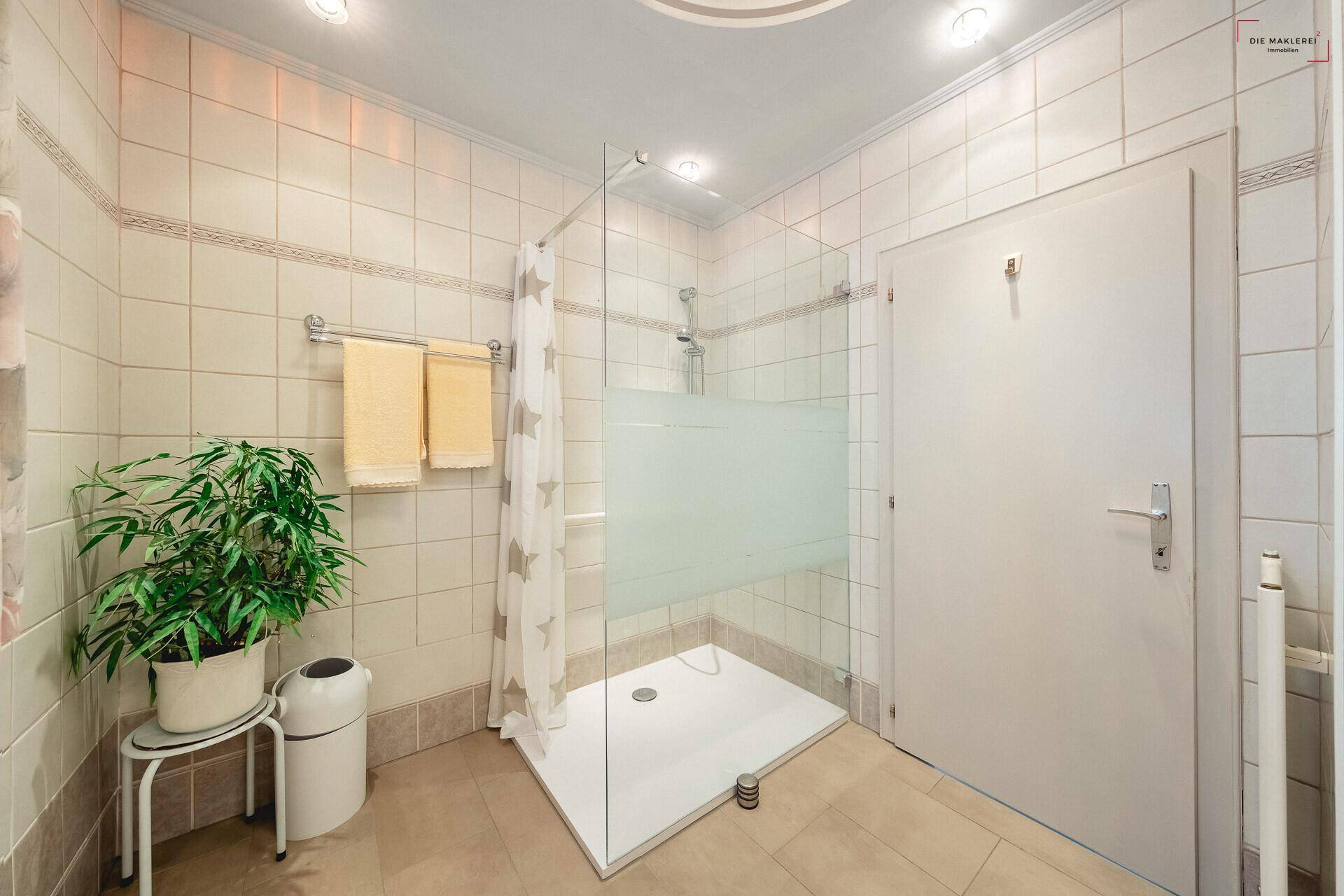 Gefliestes Badezimmer mit einer modernen Duschkabine und hellen Wand- und Bodenfliesen.