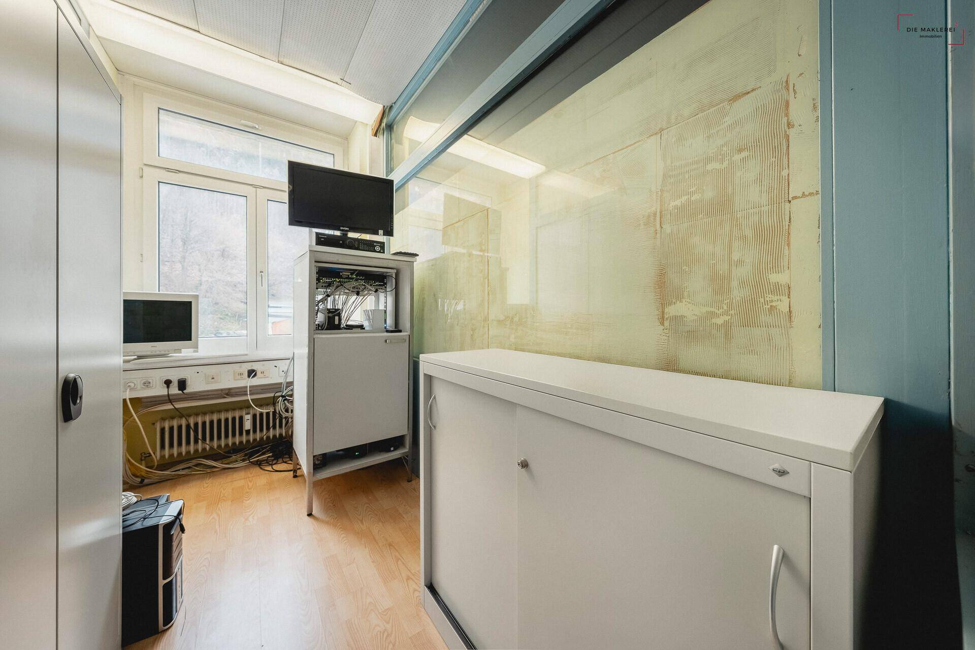 Kleiner Technikraum mit Computern, Schränken und einem Fenster, ausgestattet für IT-Infrastruktur.