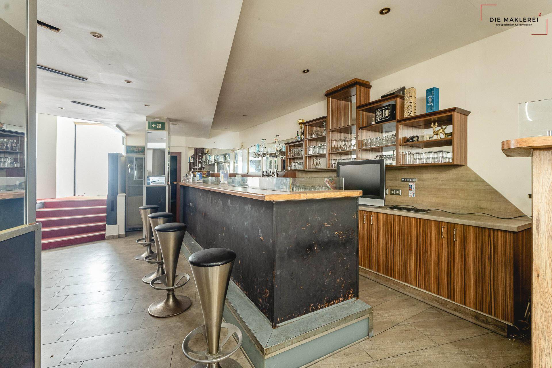 Lange Bartheke mit Barhockern und Holzverkleidung, die zu einem roten Treppenaufgang führt.