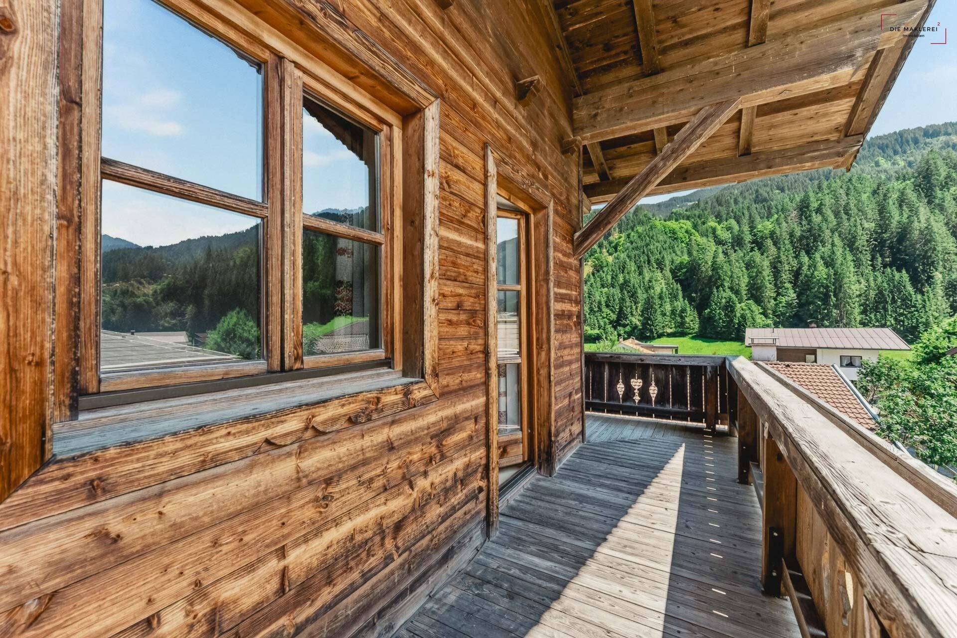 Geräumiger Holzbalkon mit traditionellem Geländer und weitem Blick ins Grüne und die Berge.
