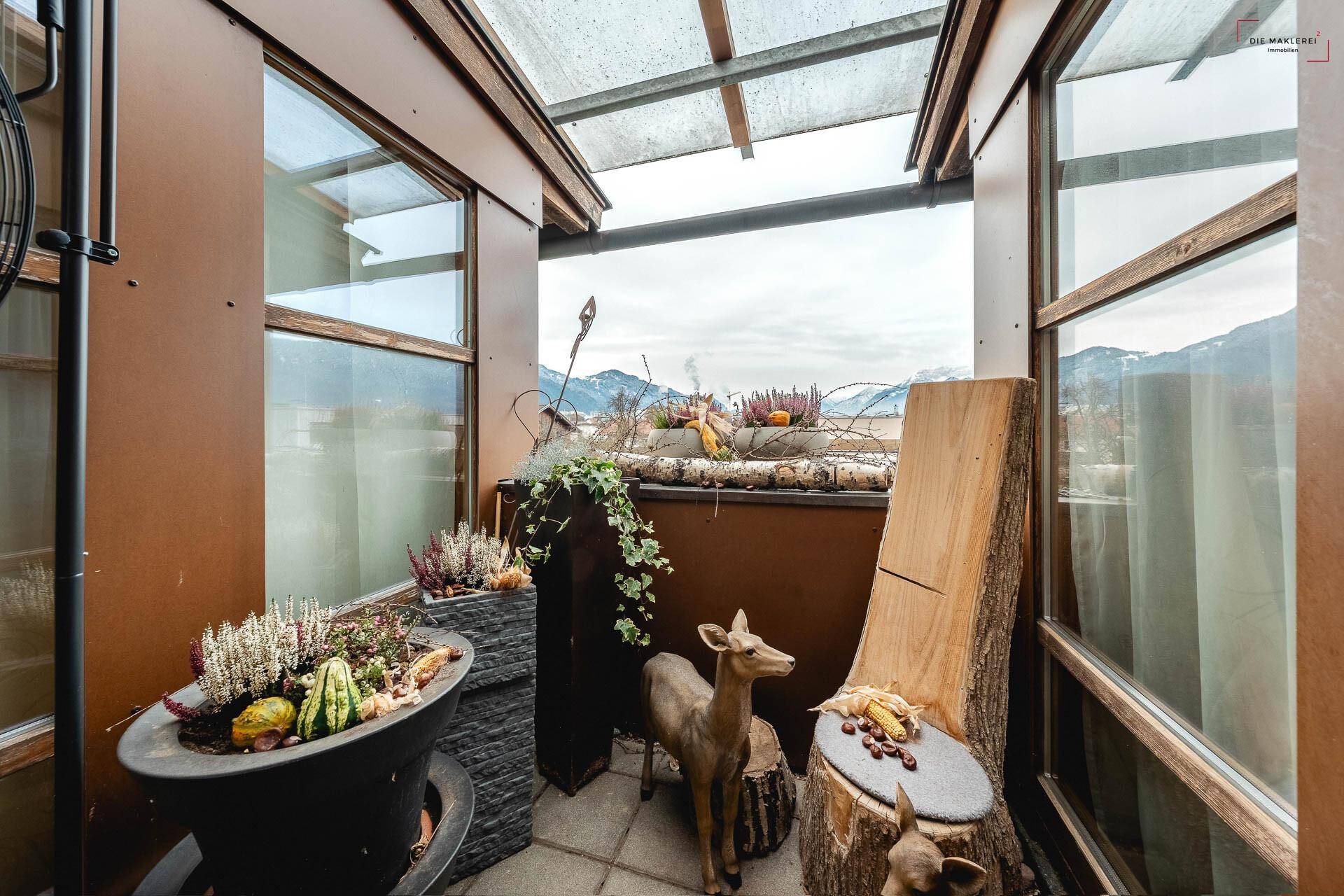 Überdachter Balkon mit Pflanzen, Dekoration und Panoramablick auf die umliegende Berglandschaft.