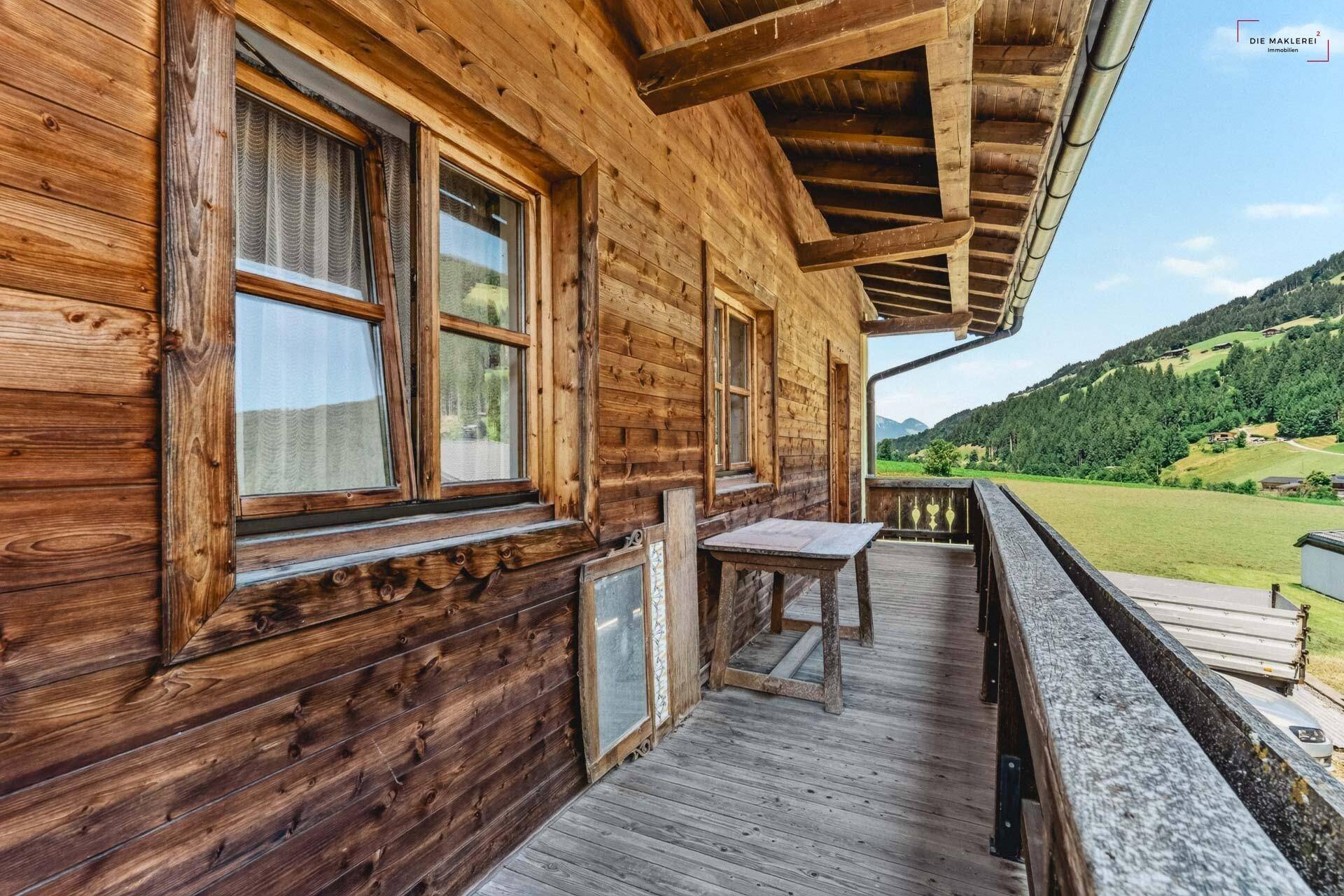Langer Holzbalkon mit traditionellem Geländer und weitem Blick auf die grüne Landschaft und Berge.
