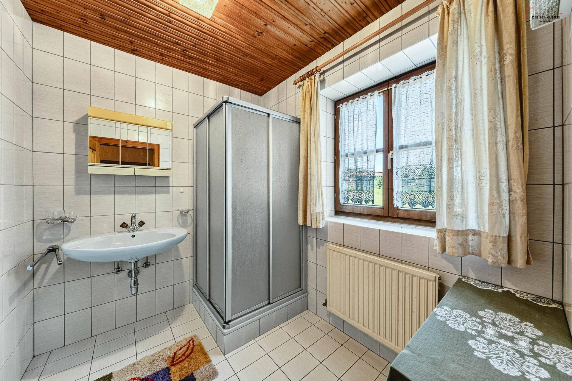 Gefliestes Badezimmer mit Duschkabine, Waschbecken, Spiegelschrank und Holzdecke.