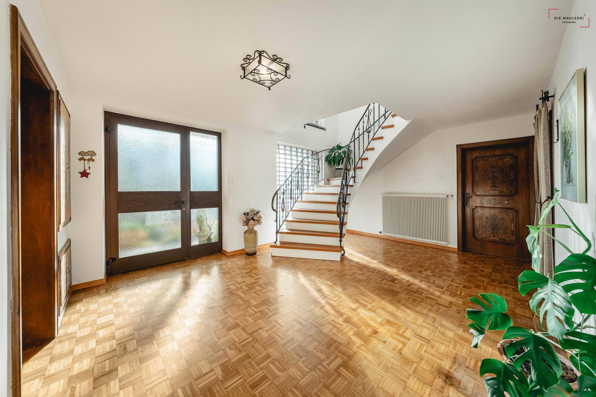 Heller Eingangsbereich mit Parkettboden, einer eleganten Treppe und viel natürlichem Licht.