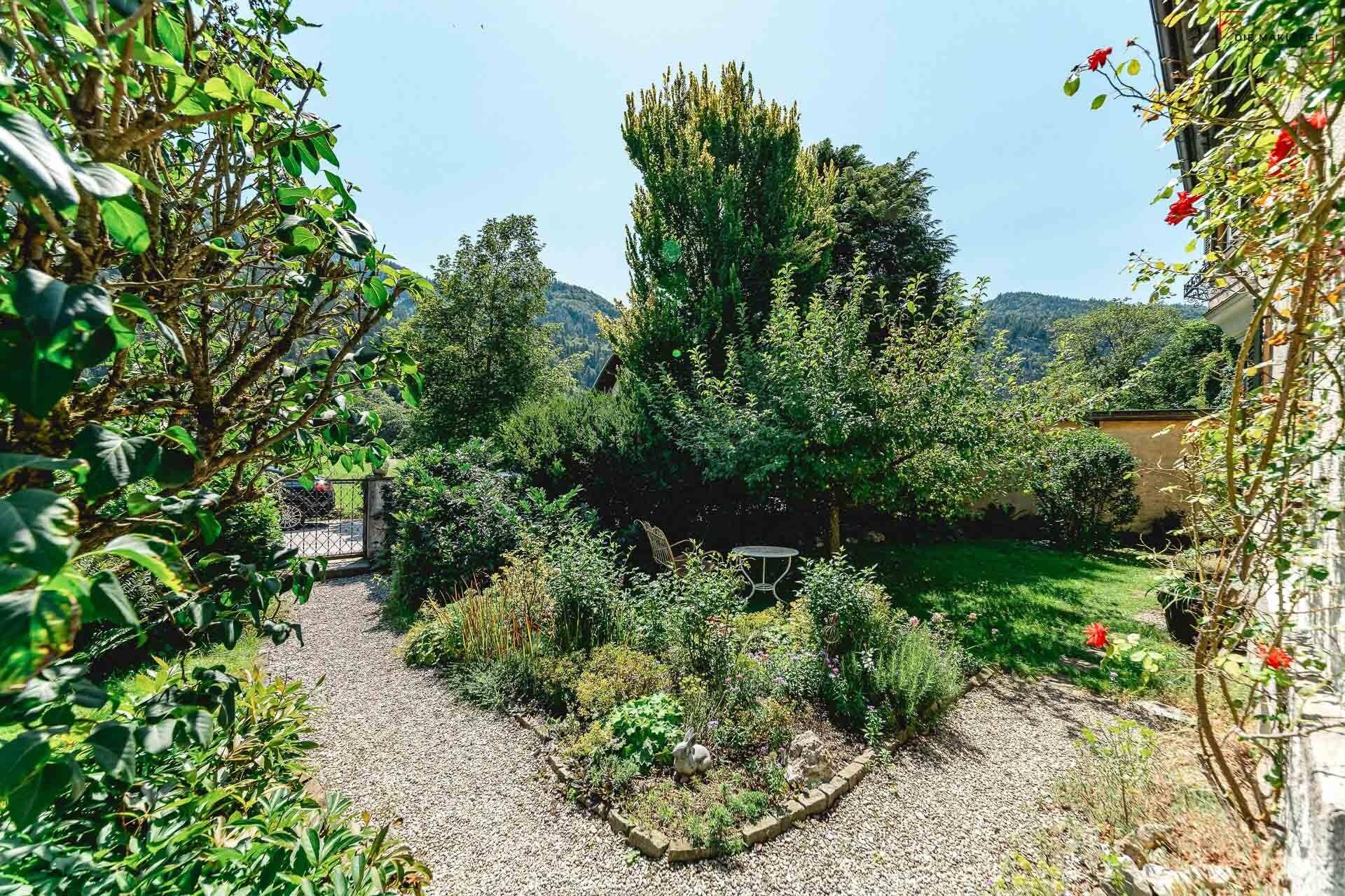 Idyllischer Gartenweg mit Kies und üppiger Bepflanzung, umgeben von hohen Bäumen.