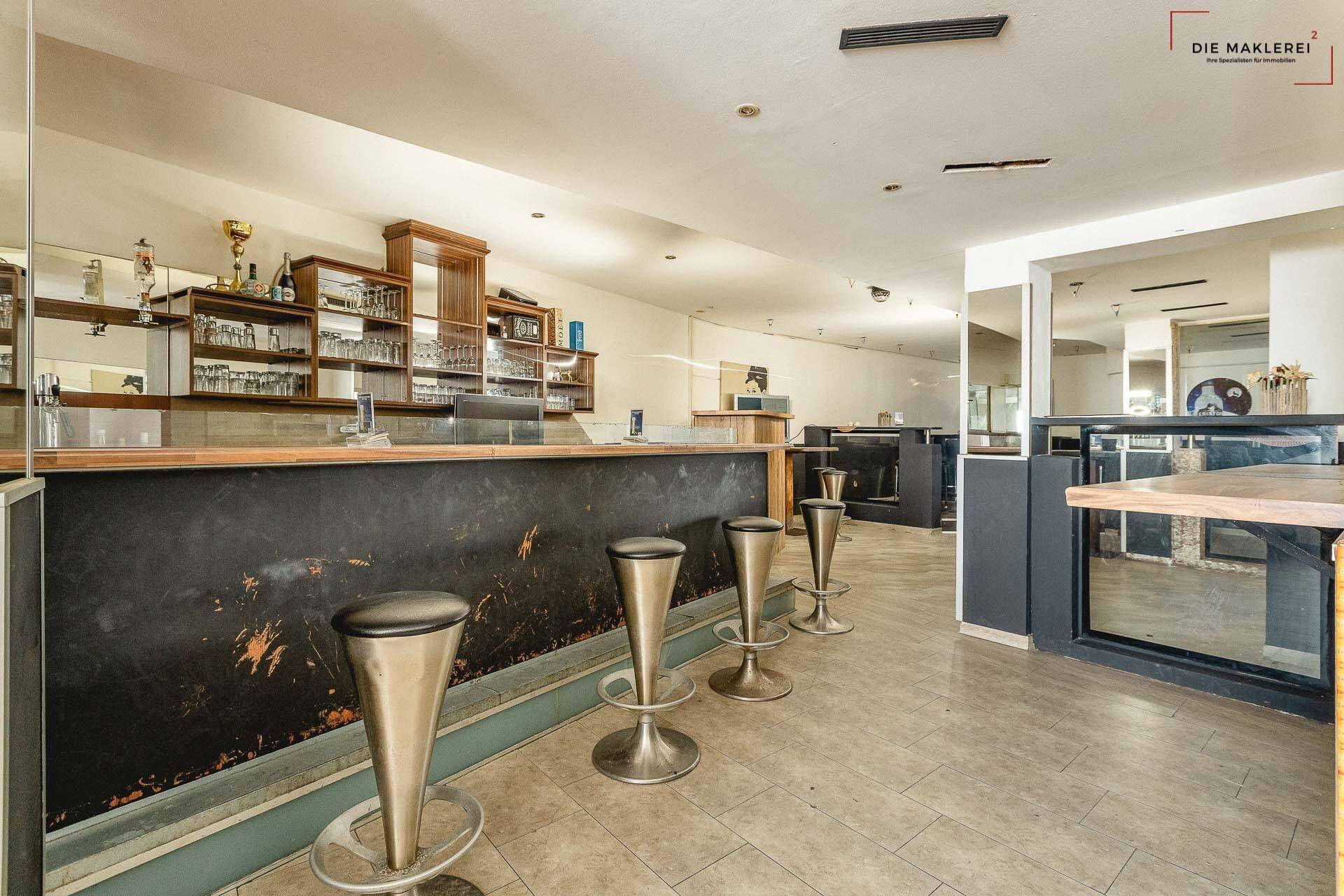Geräumiger Barbereich mit mehreren Barhockern, einer langen Theke und gefliestem Boden.