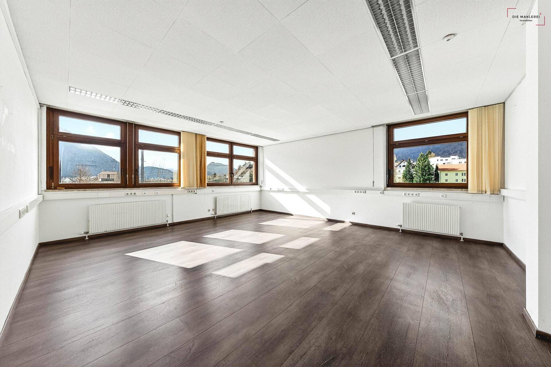 Großer, heller Büroraum mit Laminatboden, weißen Wänden und Fenstern, die einen weiten Bergblick ermöglichen.