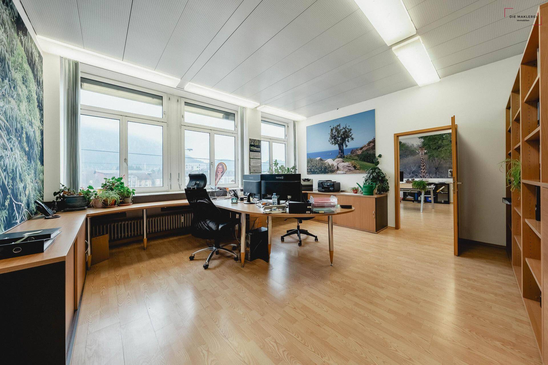 Geräumiges Büro mit Laminatboden, großen Fenstern und Blick auf die Umgebung, ausgestattet mit Holzmöbeln.