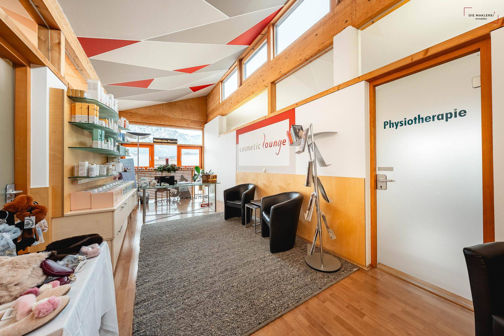 Empfangsbereich mit Teppichboden, bequemen Sesseln und Blick auf den Verkaufsbereich und die Berge.