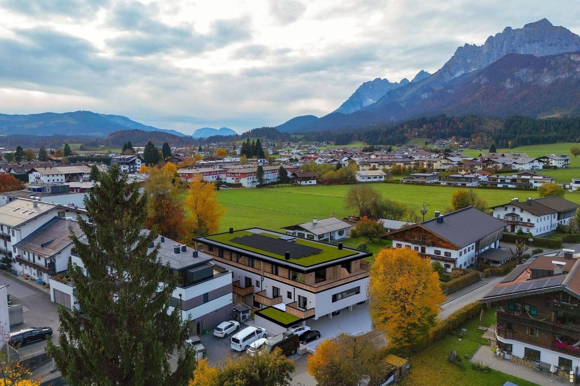 Luftaufnahme eines modernen Gebäudes mit Gründach, umgeben von ländlicher Landschaft und Bergen.