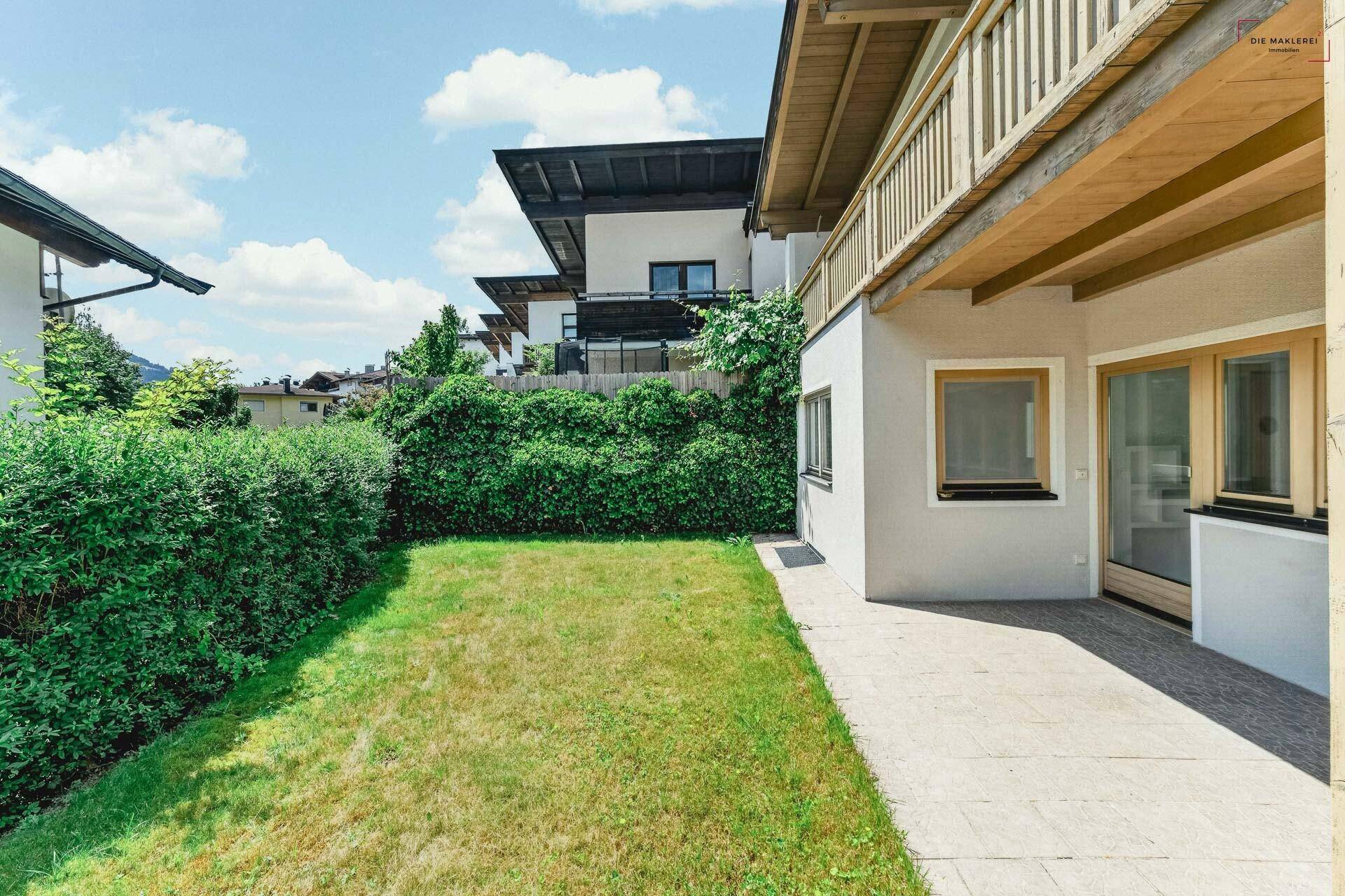 Seitlicher Gartenbereich mit Rasen, Hecke und gepflastertem Weg am Haus.