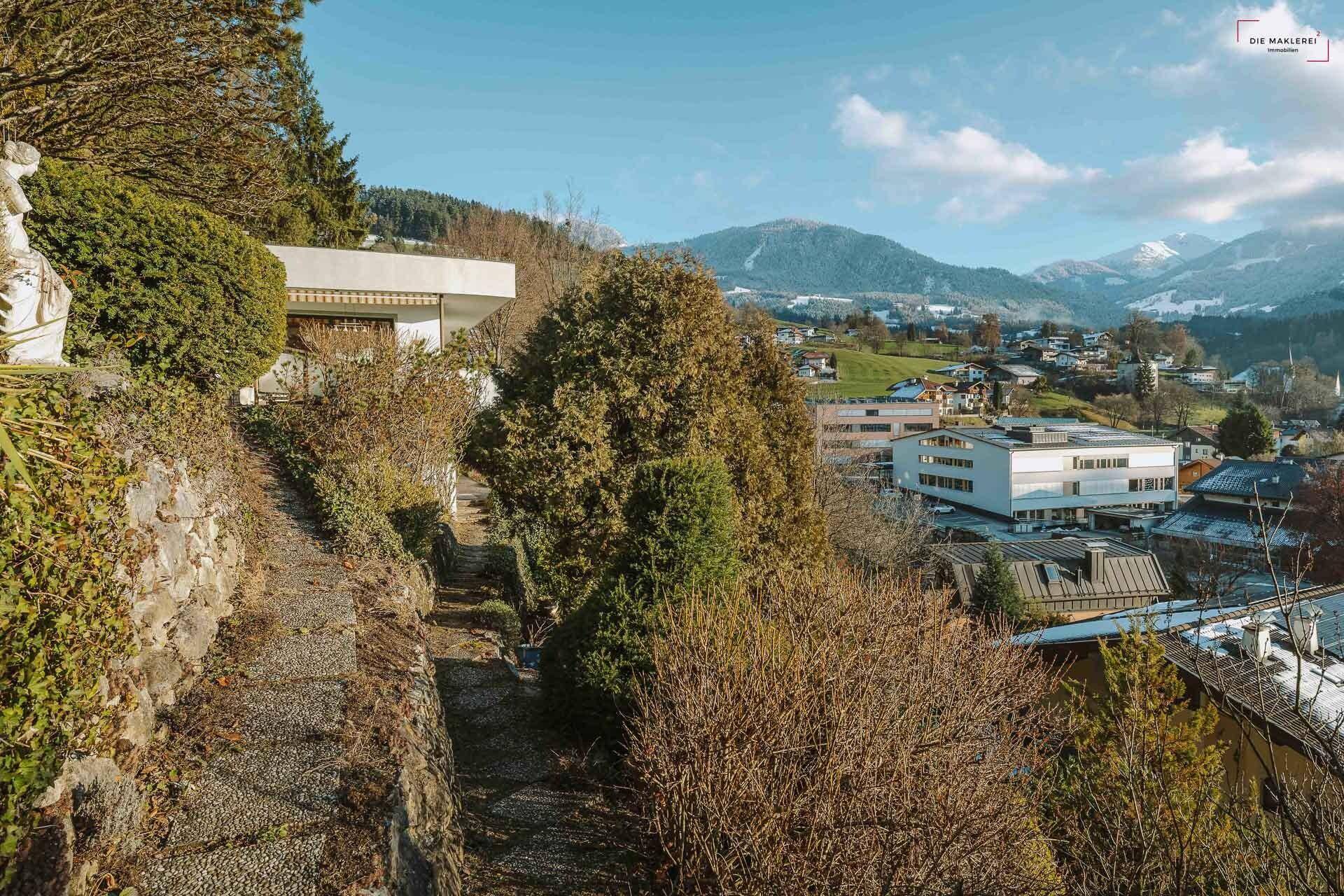 Idyllischer Gartenweg am Hang mit üppiger Vegetation und weitem Blick auf die Umgebung.
