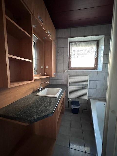 Badezimmer mit Badewanne, Fenster und Holzmöbeln, ausgestattet mit einem Waschbecken.