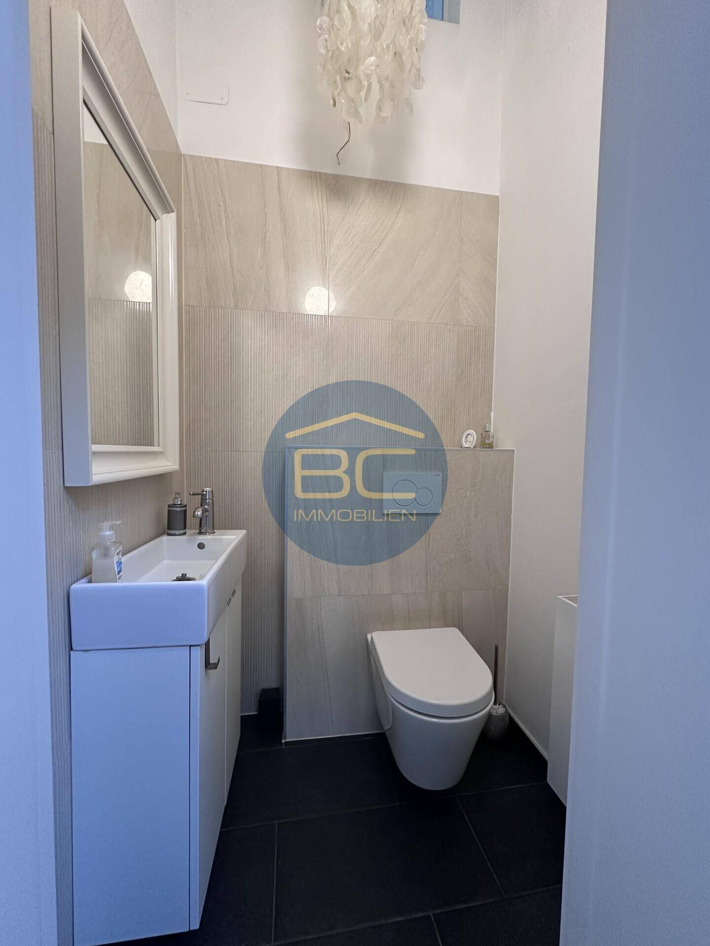 Helles Gäste-WC mit wandhängender Toilette, kleinem Waschbecken und modernen Fliesen.