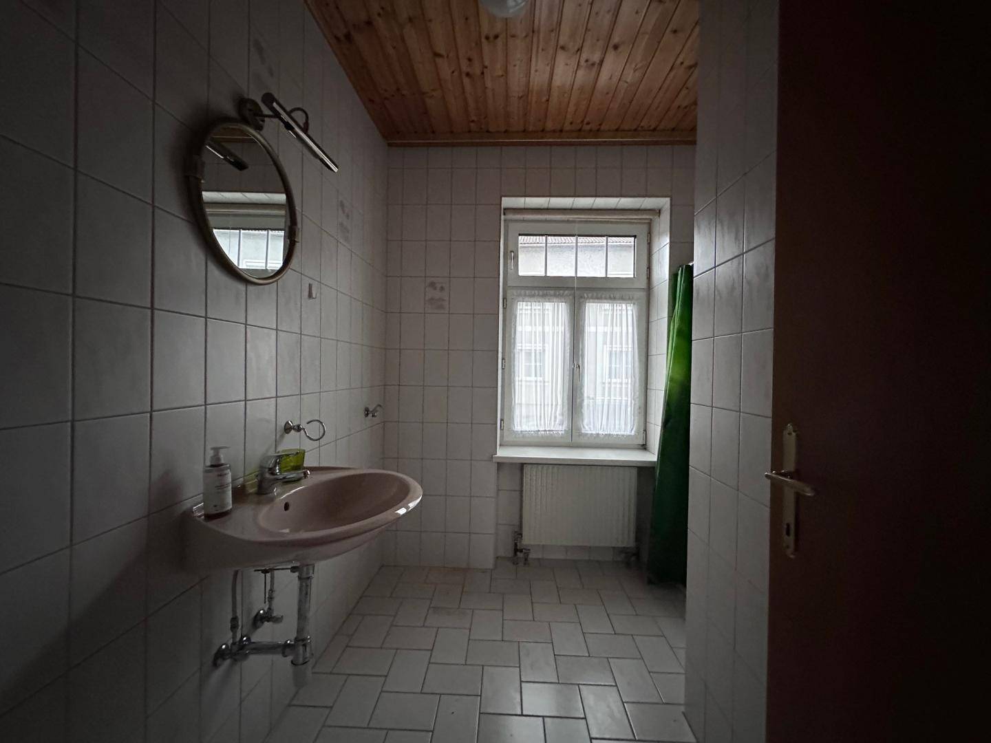 Badezimmer mit Fliesenboden, Holzdecke und einem Fenster für natürliche Belüftung.