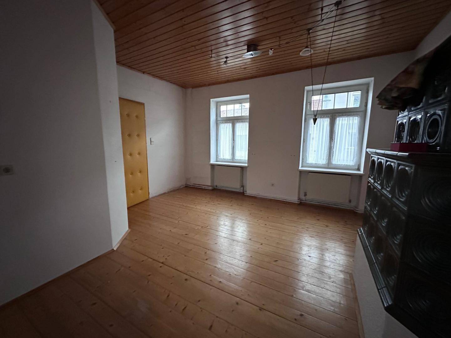 Heller Raum mit Holzdielenboden und einem traditionellen Kachelofen.