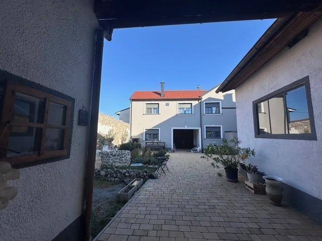 Blick durch einen überdachten Gang auf den gepflasterten Innenhof und die Rückseite des Hauses.