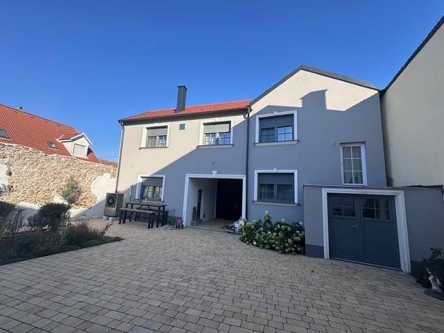 Rückseite des Hauses mit gepflastertem Innenhof, Sitzbereich und Zugang zu einem überdachten Bereich.