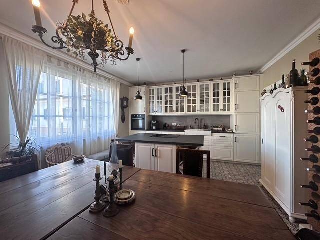 Gemütliche Wohnküche mit großem Esstisch, weißer Einbauküche und traditionellem Kronleuchter.