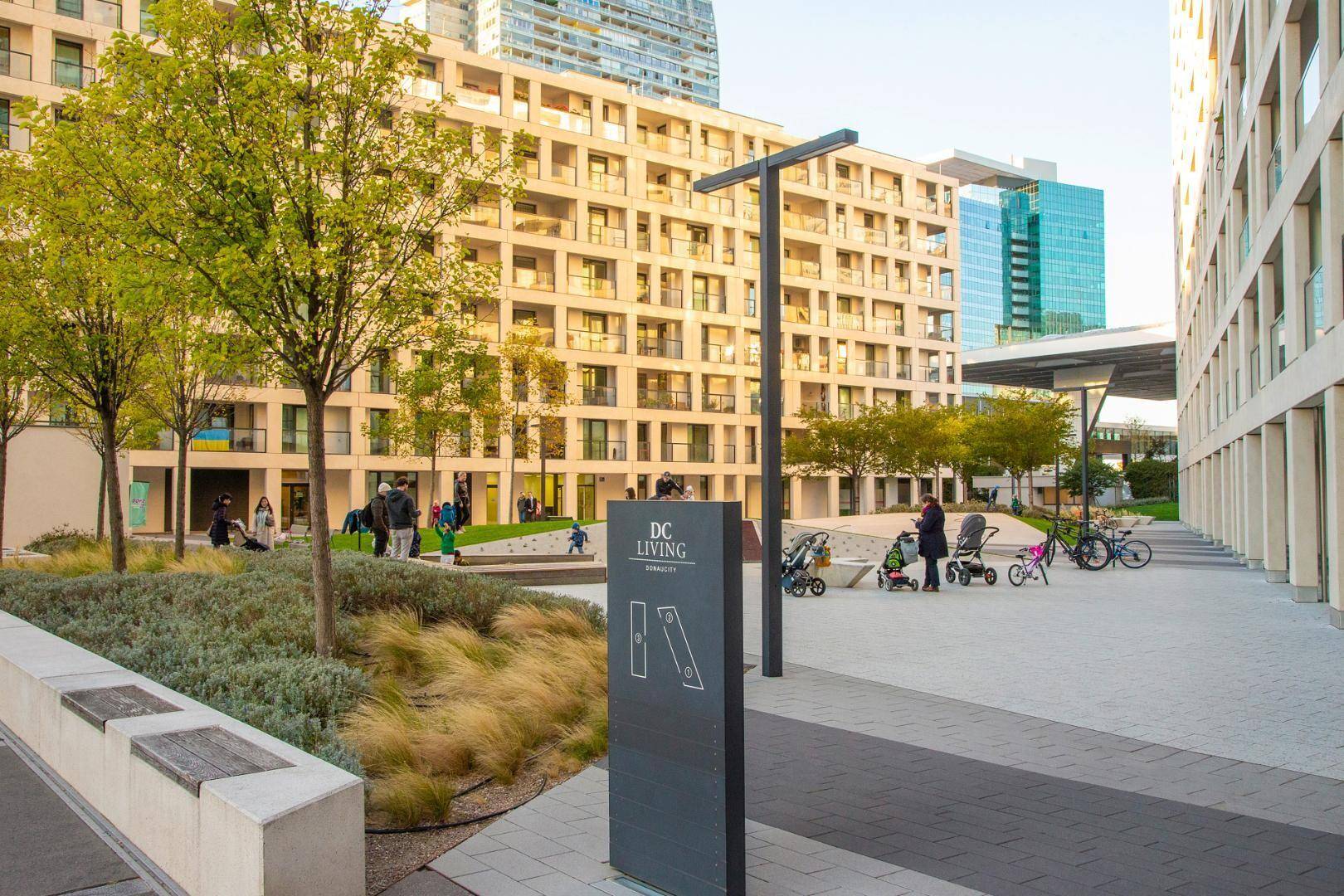 Neubau-Wohnkomplex mit modernen Gebäuden, Grünflächen und einem Hinweisschild für DC Living.