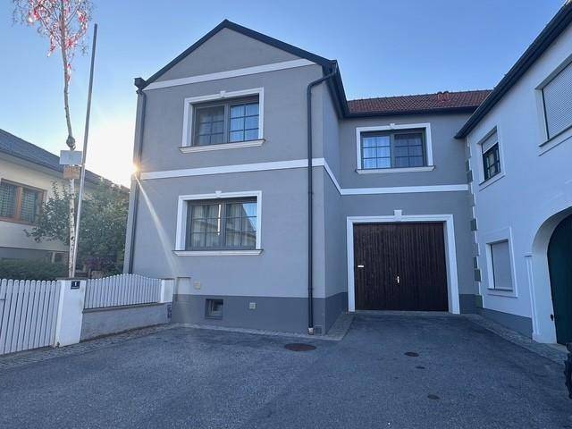 Vorderansicht des Hauses mit grauer Fassade, weißen Akzenten und integrierter Garage.