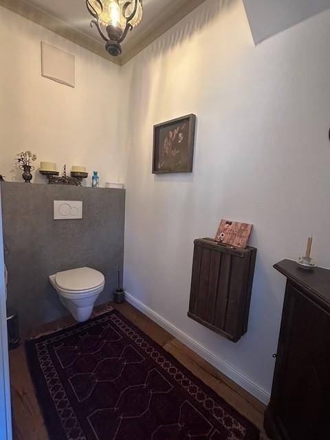 Gäste-WC mit Wand-WC, Holzboden und traditionellem Teppich.