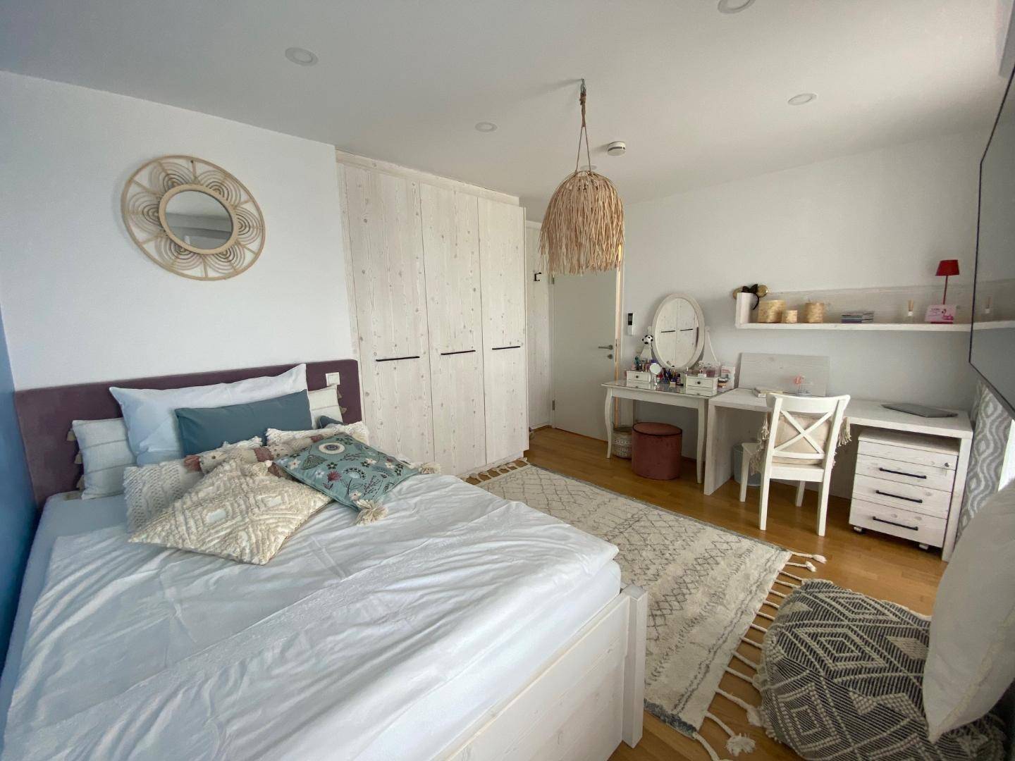 Helles Schlafzimmer mit Holzboden, weißem Kleiderschrank und Schminktisch.
