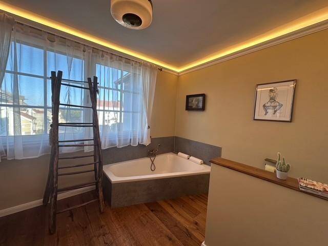 Badezimmer mit Badewanne, Holzboden und großem Fenster.