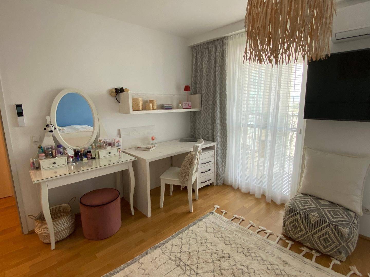 Helles Schlafzimmer mit Schreibtisch, Schminktisch und großen Fenstern.
