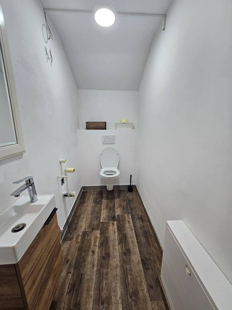 Modernes Gäste-WC im Keller mit Holzoptikboden und schlichtem Waschbecken.