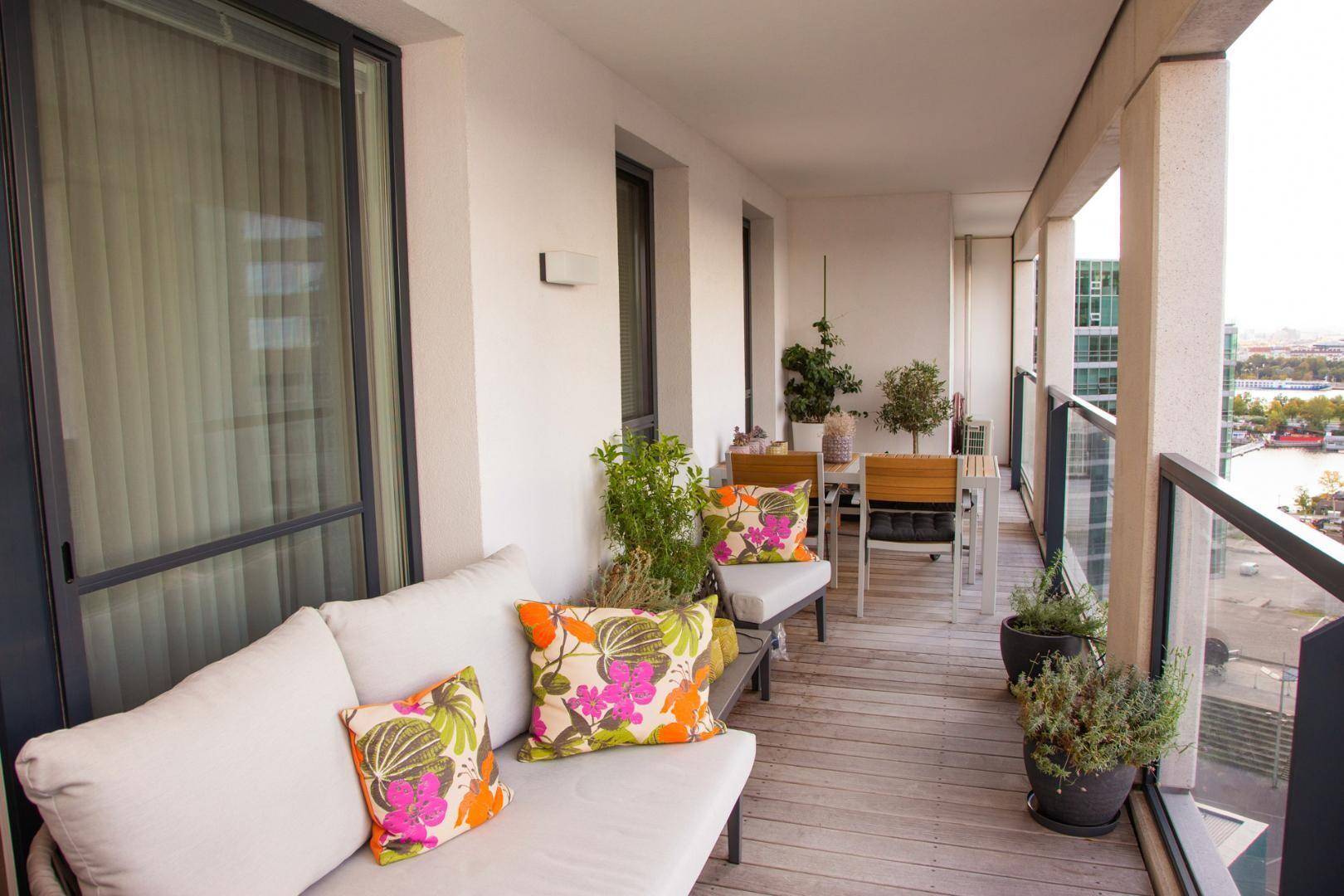 Geräumiger Balkon mit Holzdeck, bequemen Gartenmöbeln und Pflanzen.