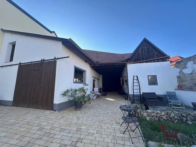 Gepflasterter Innenhof mit überdachtem Durchgang, Sitzgelegenheiten und rustikalen Holztüren.