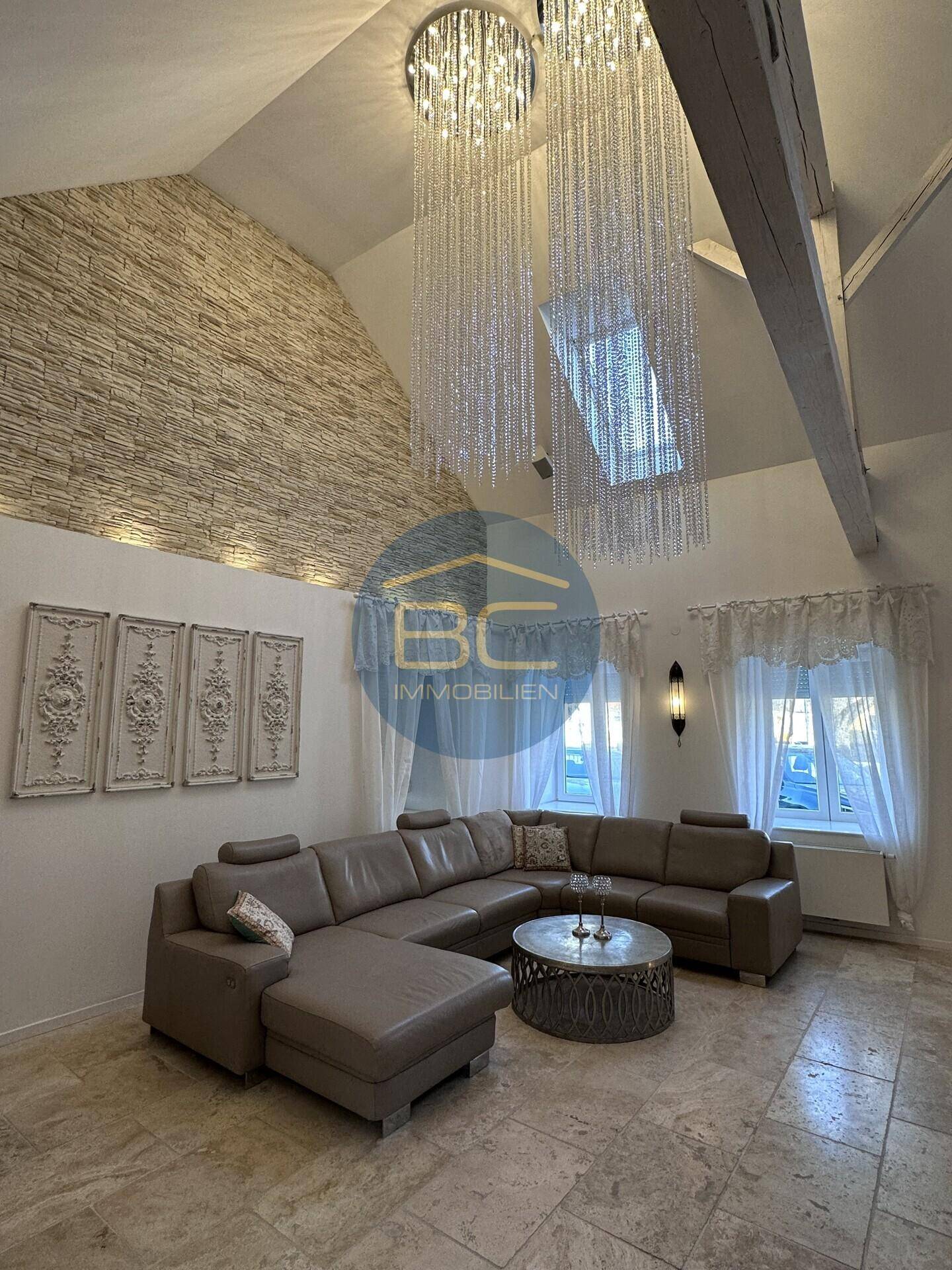 Elegantes Wohnzimmer mit hoher Decke, freiliegenden Balken und beeindruckenden Kronleuchtern.