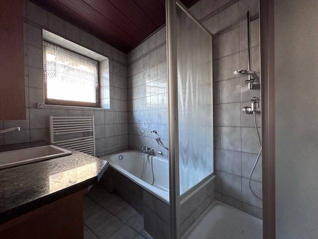 Badezimmer mit Badewanne, Duschbereich und Fenster für Tageslicht.