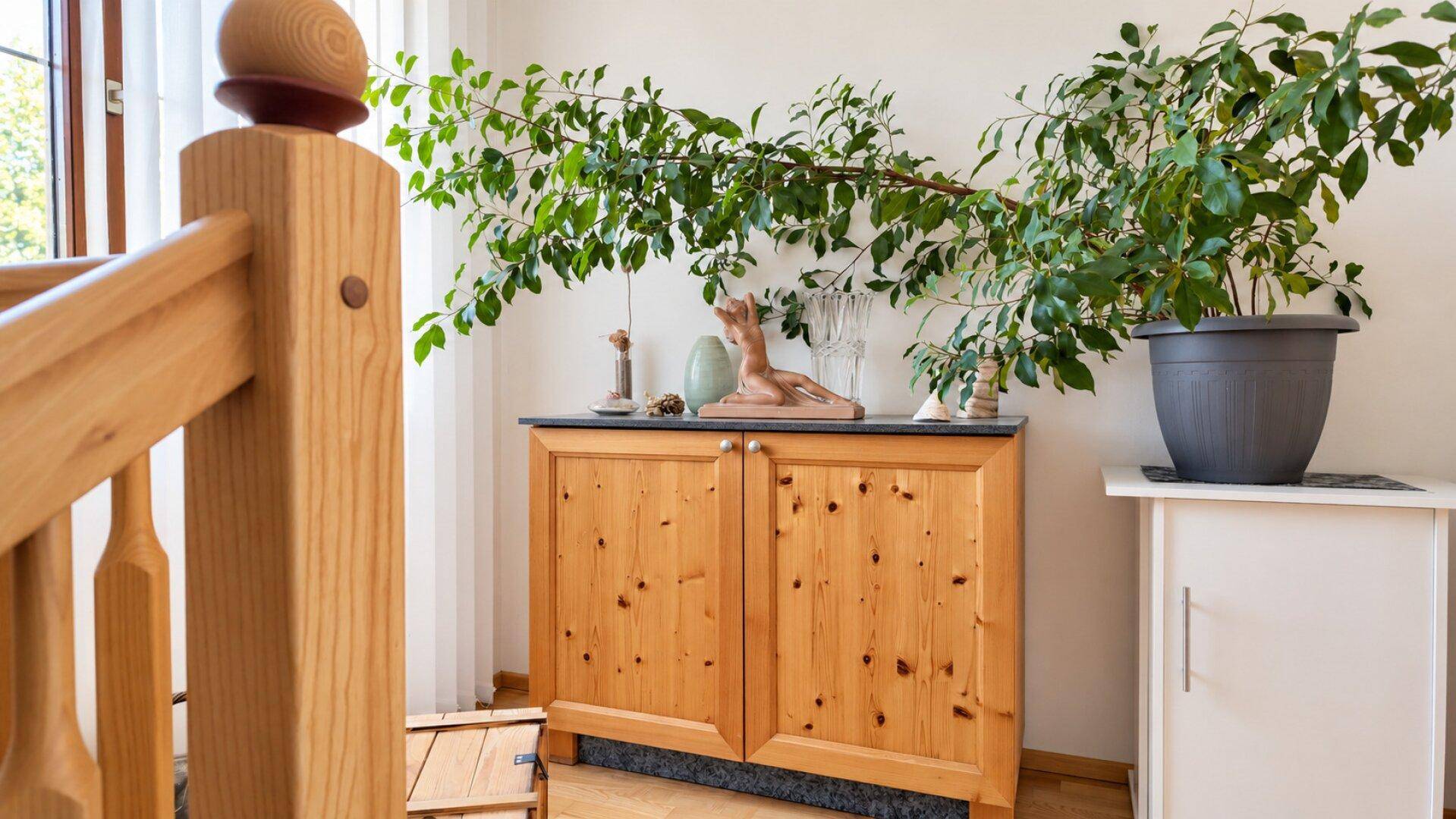 Heller Flur mit Holzschrank, Zimmerpflanze und Blick auf eine Holztreppe im Landhausstil.