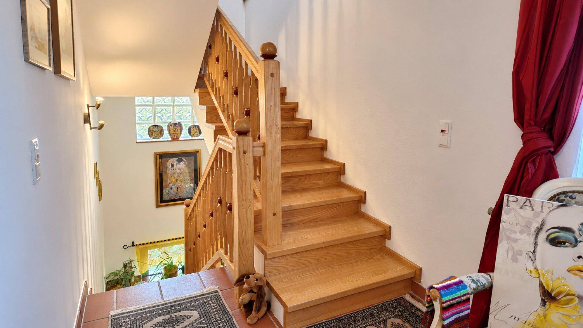 Holztreppe mit Geländer führt in die obere Etage, beleuchtet durch ein Fenster mit Glasbausteinen.