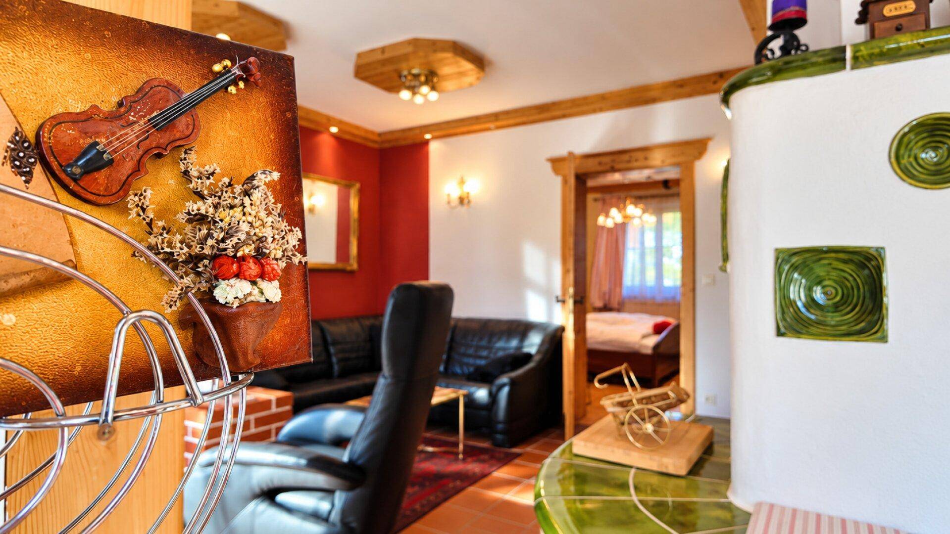 Gemütliches Wohnzimmer mit Kachelofen, Ledersofas und traditioneller Dekoration in warmen Farben.