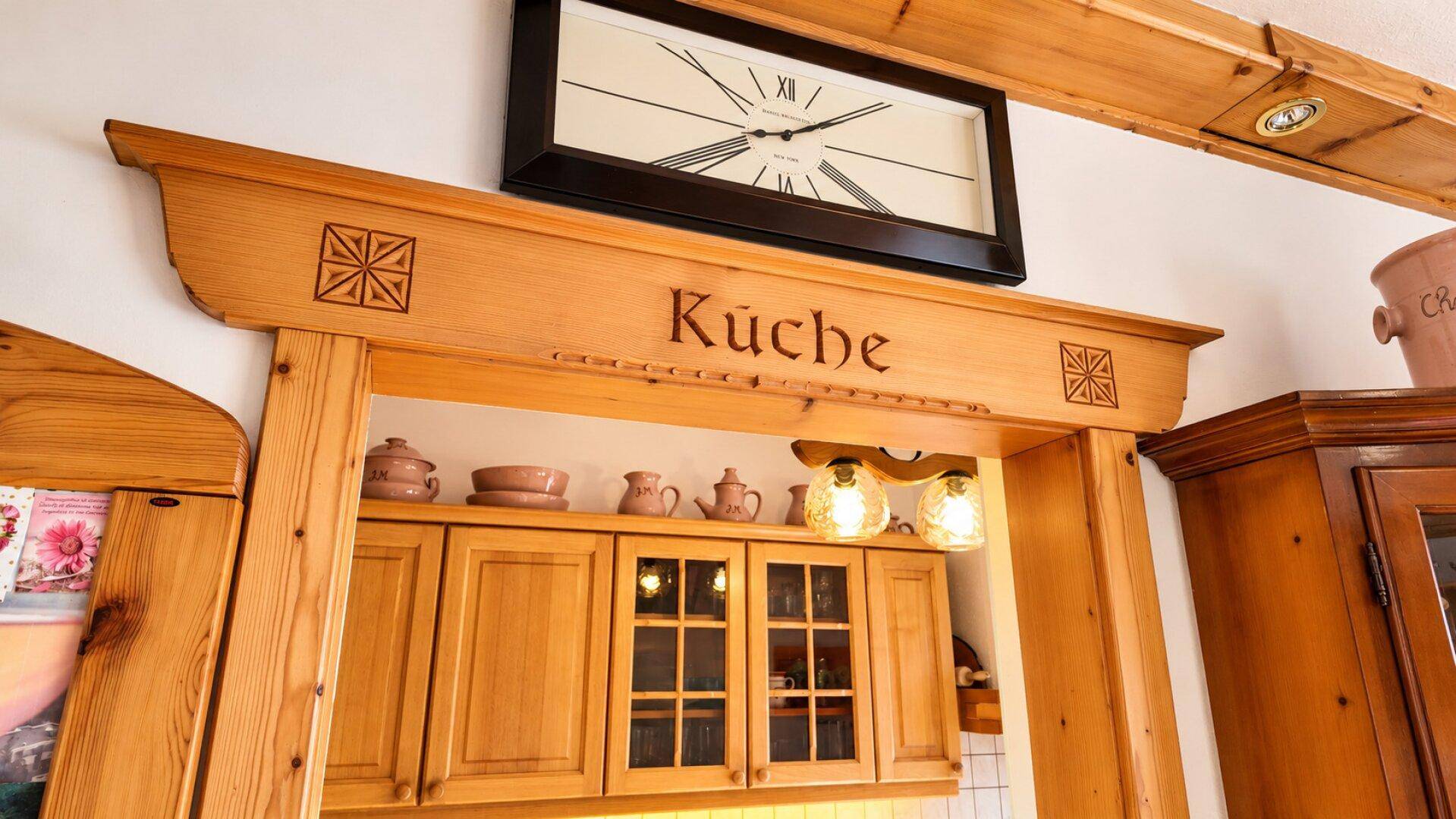 Rustikaler Holzbogen mit der Aufschrift "Küche" über dem Eingang zu einem traditionellen Küchenbereich.