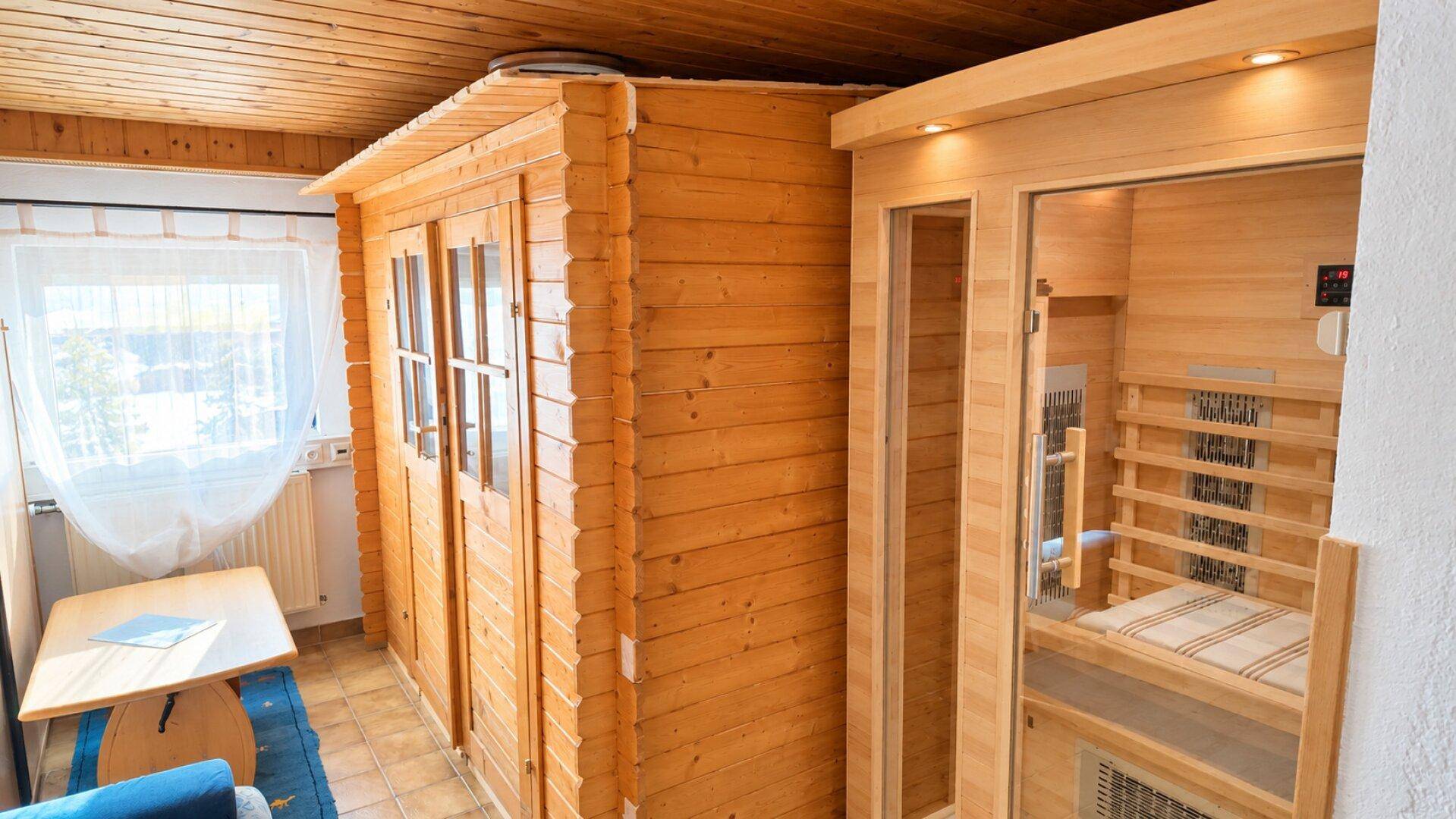 Raum mit einer Infrarotsauna und einer weiteren Holzkabine, umgeben von Holzdecken und einem Fenster.