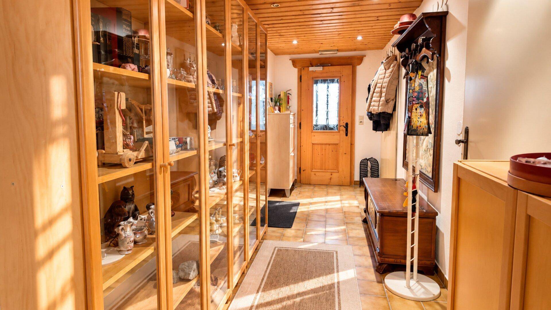 Langer Flur mit Holzdecke, Vitrinenschränken und einem Eingangsbereich mit Garderobe.