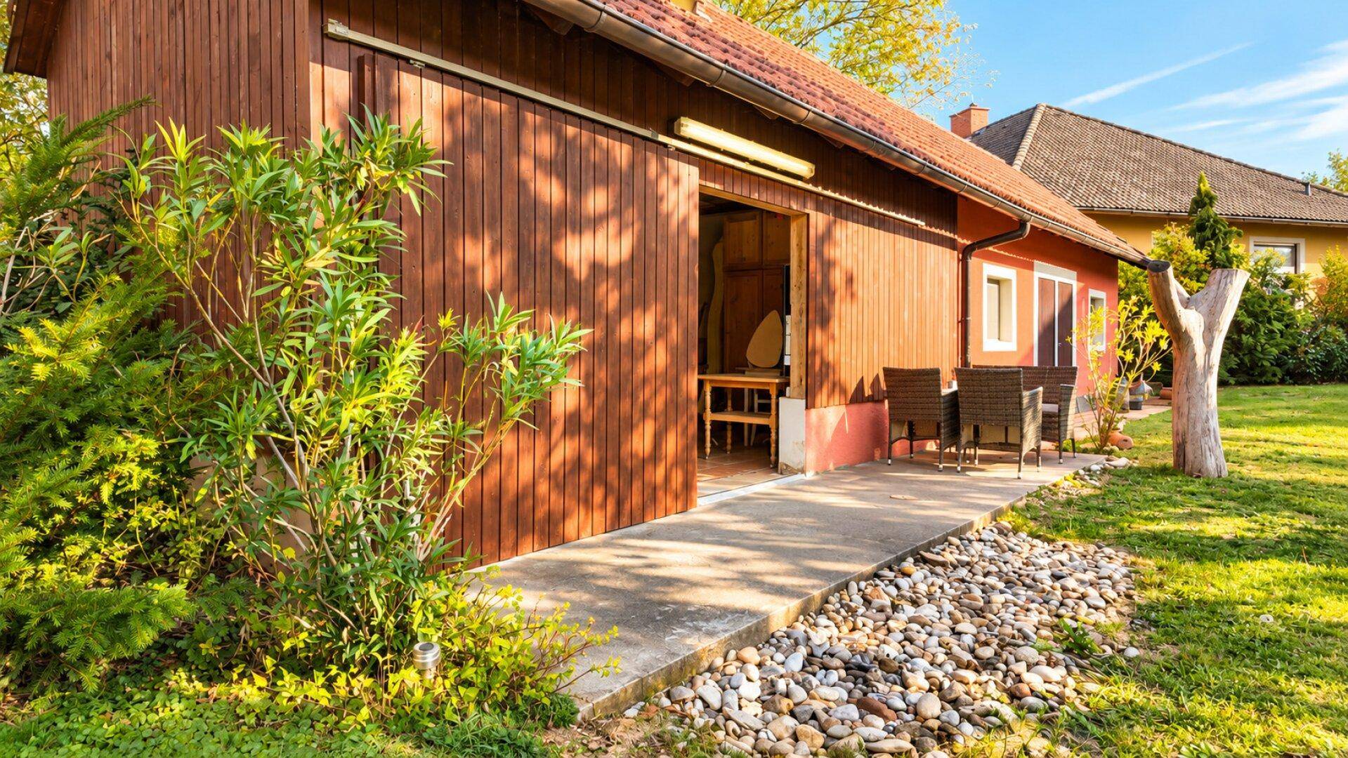 Eine rustikale Holzscheune mit einer kleinen gepflasterten Terrasse und Gartenmöbeln im Freien.