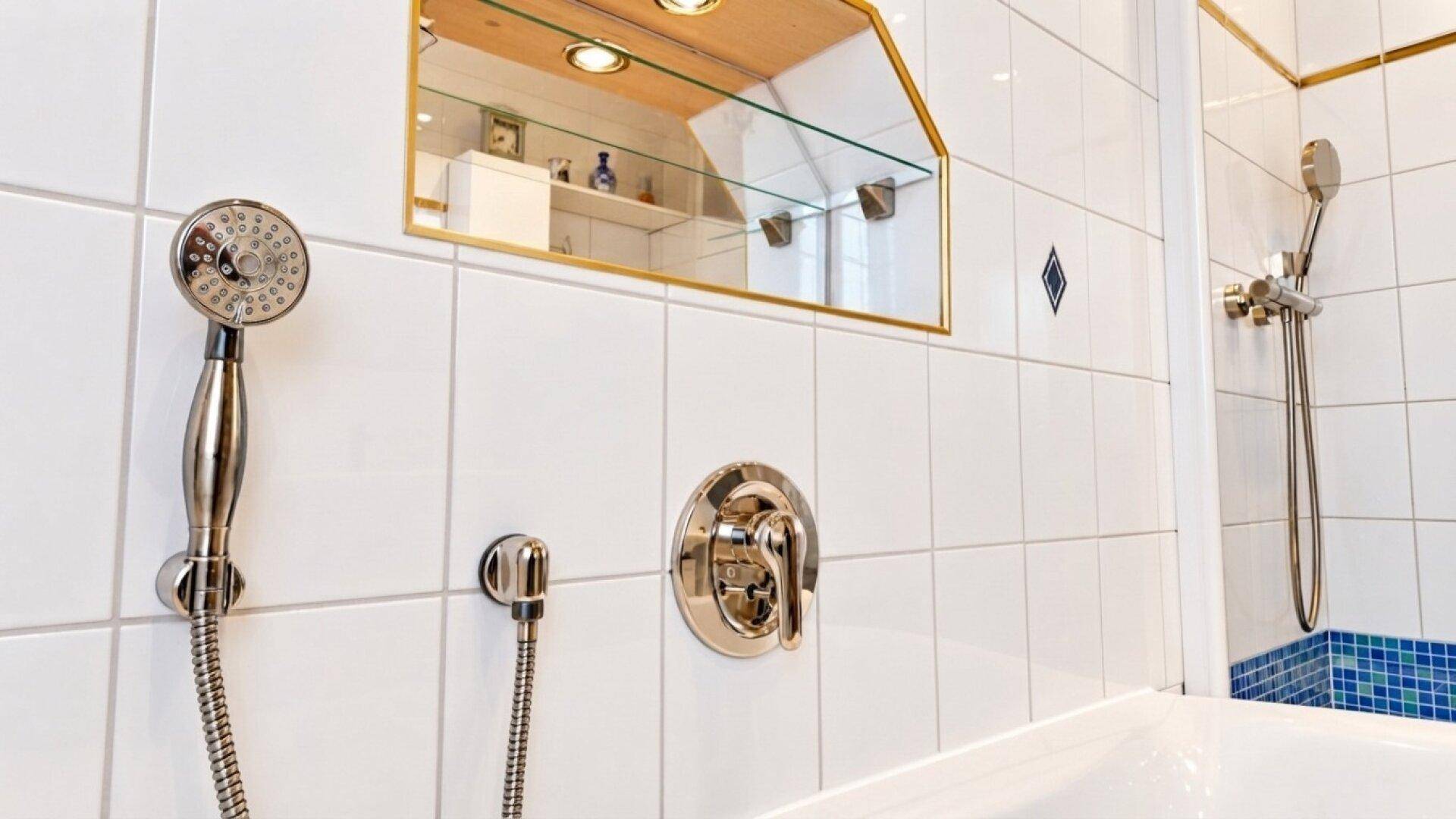 Duscharmatur und Handbrause an einer weiß gefliesten Wand mit blauen Mosaikakzenten im Badezimmer.