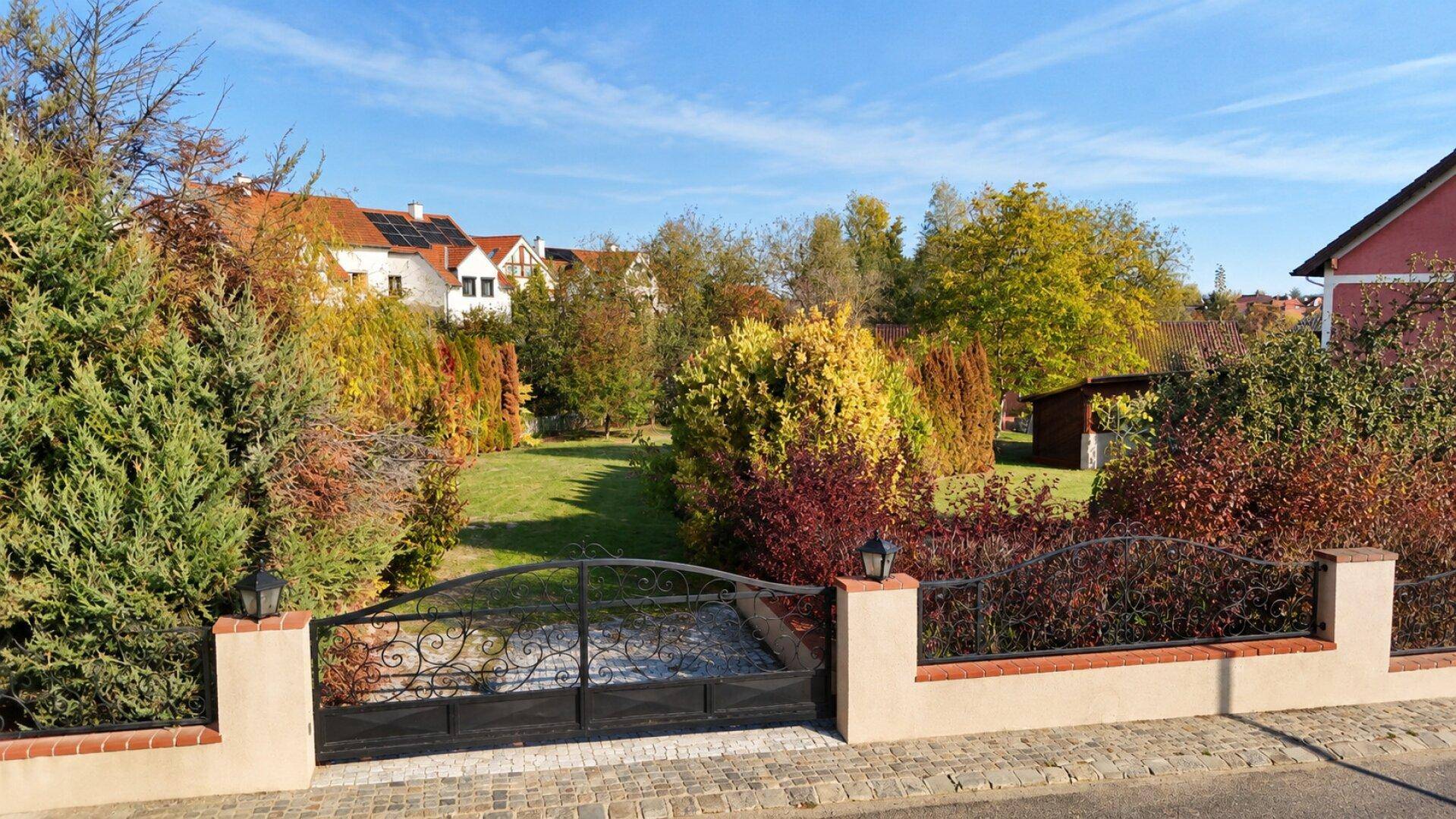 Eingangsbereich mit schmiedeeisernem Tor und Blick auf den weitläufigen, grünen Vorgarten des Anwesens.