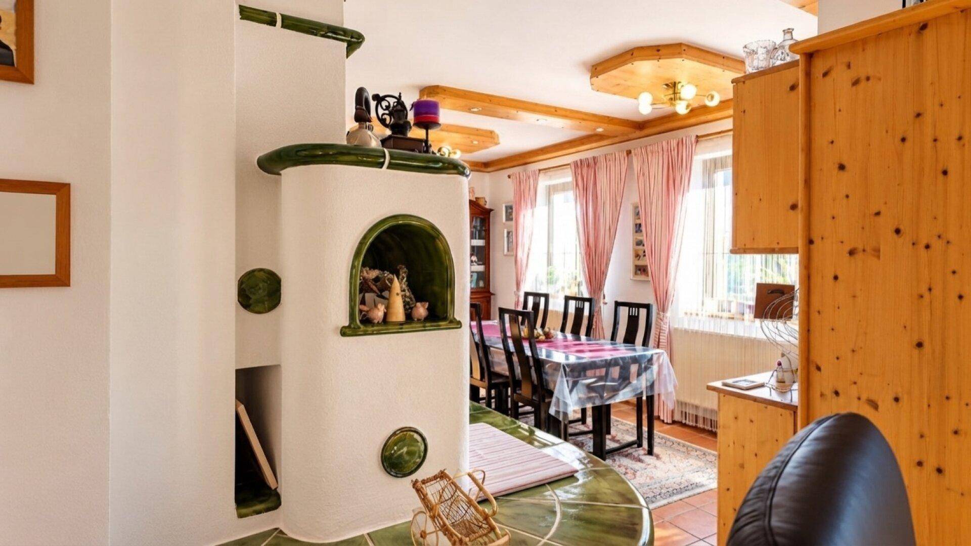 Offener Wohn-Essbereich mit traditionellem Kachelofen, Holztisch und rustikalen Elementen.